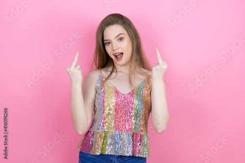 Pretty redhead woman wearing a shiny top standing over pink background showing middle finger doing fuck you bad expression, provocation and rude attitude. screaming excited photo