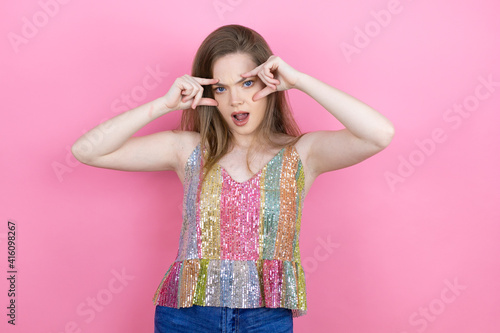 Pretty redhead woman wearing a shiny top standing over pink background Trying to open eyes with fingers, sleepy and tired for morning fatigue © Irene