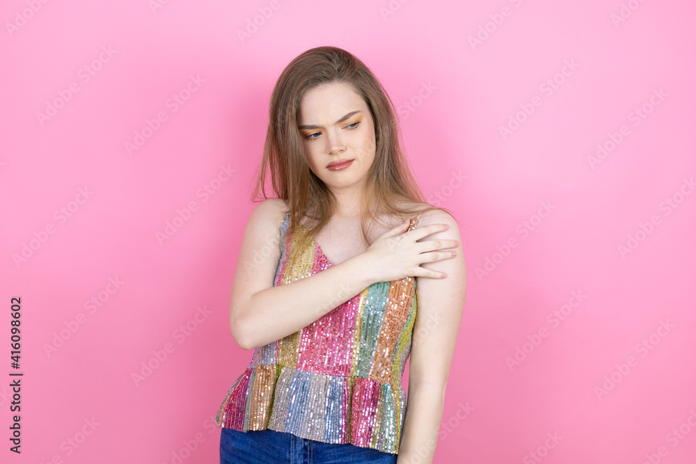 Pretty redhead woman wearing a shiny top standing over pink background with pain on her shoulder and a painful expression Pretty redhead woman wearing a shiny top standing over pink background with pain on her shoulder and a painful expression