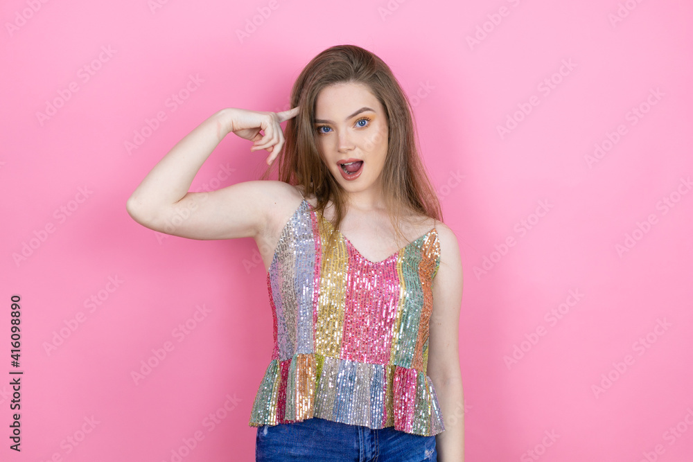 Pretty redhead woman wearing a shiny top standing over pink background surprised and thinking with her finger on her head that she has an idea. Pretty redhead woman wearing a shiny top standing over pink background surprised and thinking with her finger on her head that she has an idea.