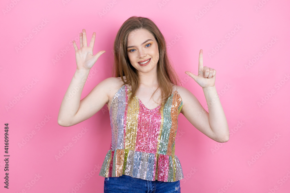 Pretty redhead woman wearing a shiny top standing over pink background showing and pointing up with fingers number seven while smiling confident and happy Pretty redhead woman wearing a shiny top standing over pink background showing and pointing up with fingers number seven while smiling confident and happy