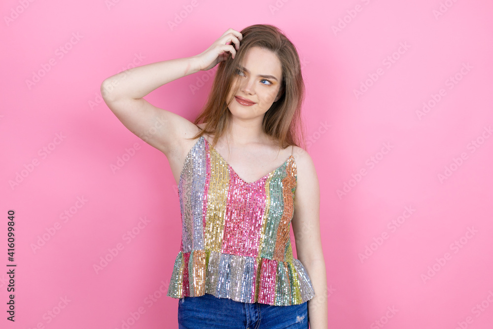 Pretty redhead woman wearing a shiny top standing over pink background confuse and wonder about question. Uncertain with doubt, thinking with hand on head Pretty redhead woman wearing a shiny top standing over pink background confuse and wonder about question. Uncertain with doubt, thinking with hand on head
