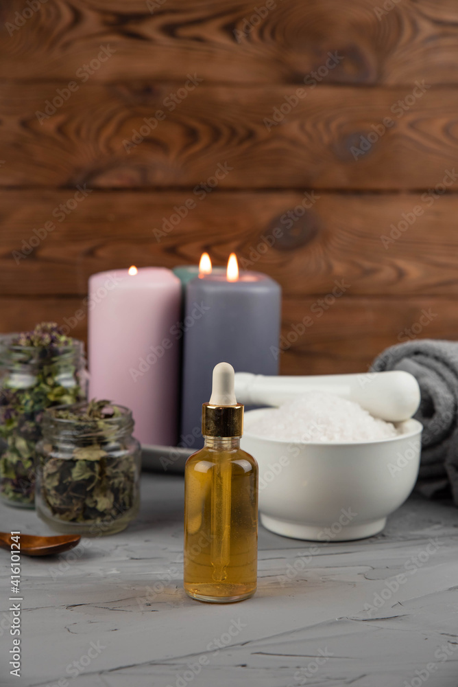 Herbal therapy, traditional medicine and homeopathy concept. Towel with salt, herbs, candles and bottle natural organic oil essence serum. Set for spa, massage and aromatherapy