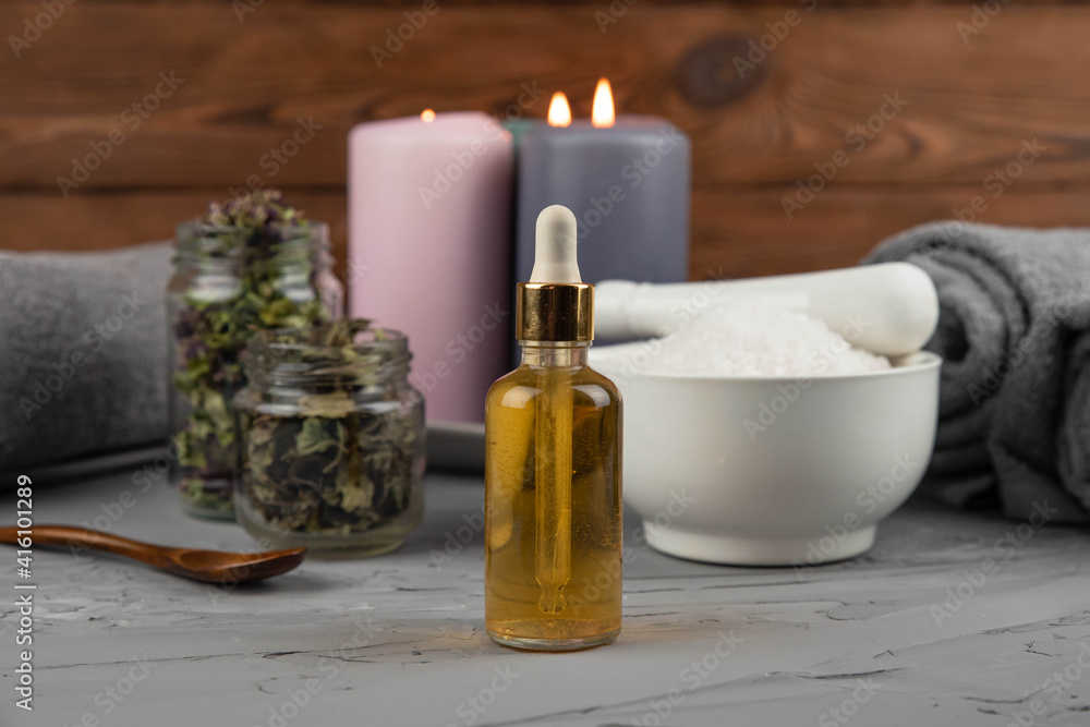 Herbal therapy, traditional medicine and homeopathy concept. Towel with salt, herbs, candles and bottle natural organic oil essence serum. Set for spa, massage and aromatherapy