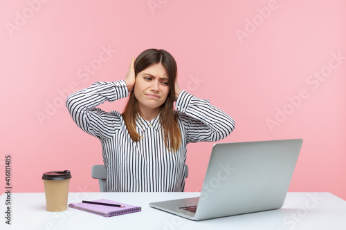 I dont hear you. Upset woman office worker covering ears and looking irritably at laptop screen, annoyed by unpleasant sound during video call. Indoor studio shot isolated on pink background