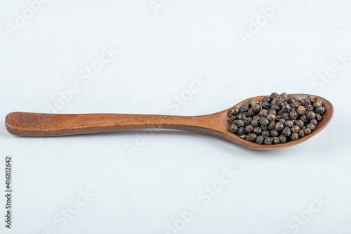 A wooden spoon full of dried pepper on a white background