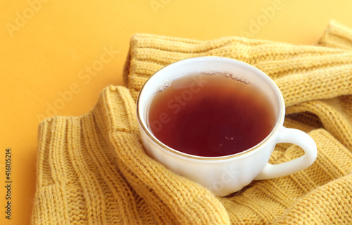A cup of hot tea in a yellow knitted sweater, top view, close-up