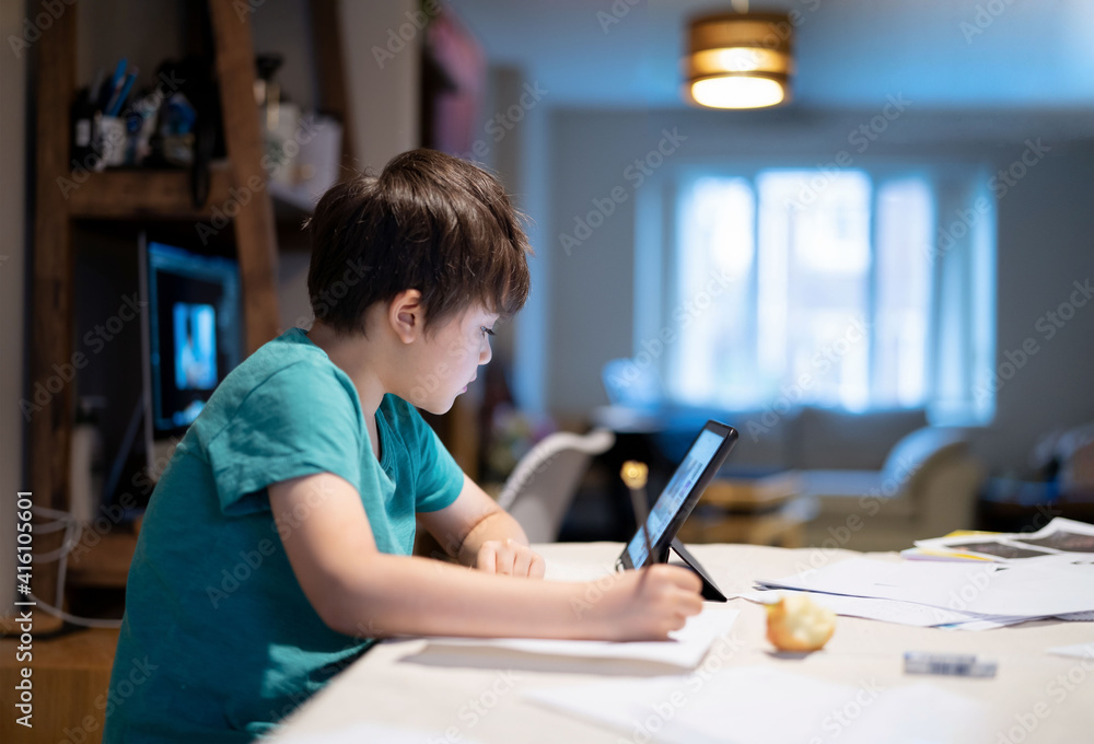 Kid holding pencil wring on paper, Child using digital tablet searching information on internet for his homework, Home schooling, E-learning online education Kid holding pencil wring on paper, Child using digital tablet searching information on internet for his homework, Home schooling, E-learning online education