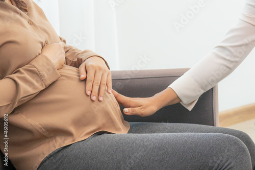 Young asian pregnant woman holding her belly while gynecologist check up the symptoms by touching  her abdomen about the pregnancy is explaining about the unborn child.