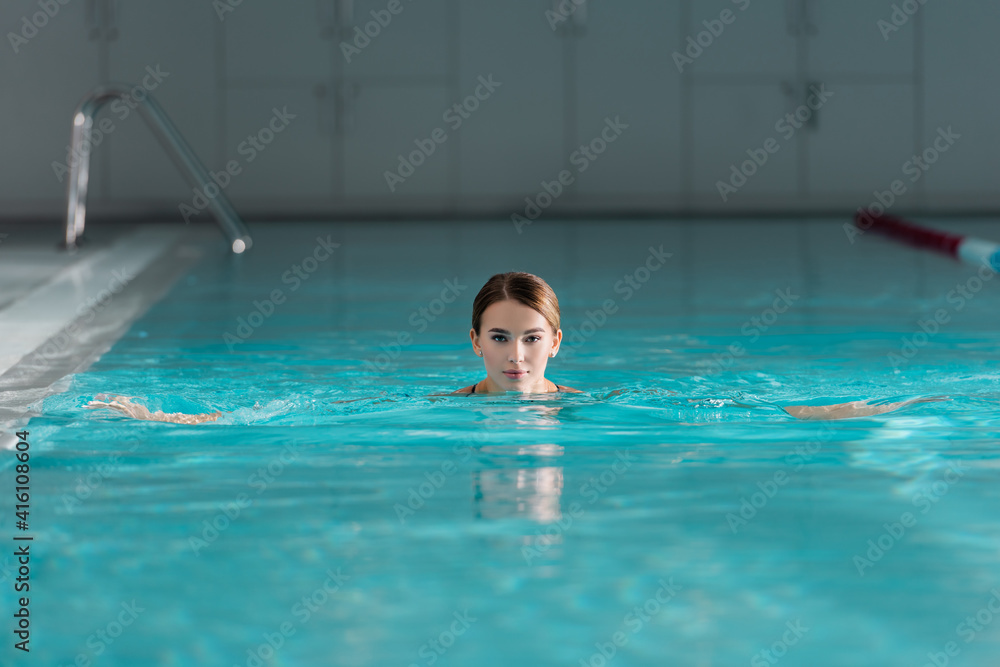 young woman looking at camera while swimming in pool of luxury spa center