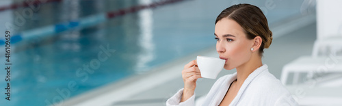 Young woman in bathrobe drinking tea near swimming pool on blurred background, banner