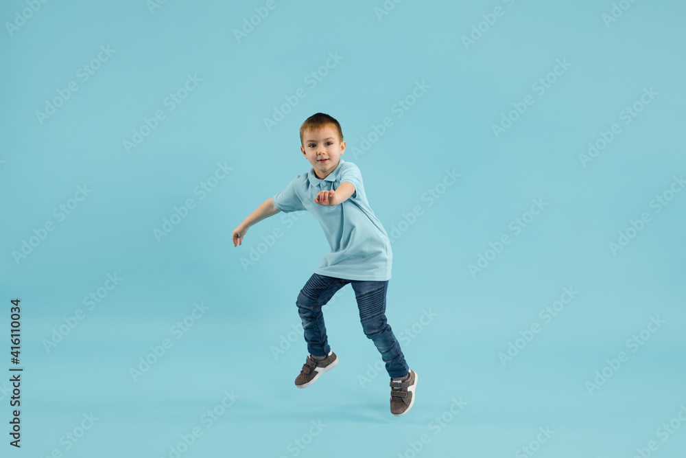 Happy, cheering. Childhood and dream about big and famous future. Pretty little boy isolated on blue studio background. Dreams, imagination, education, facial expression, emotions concept.