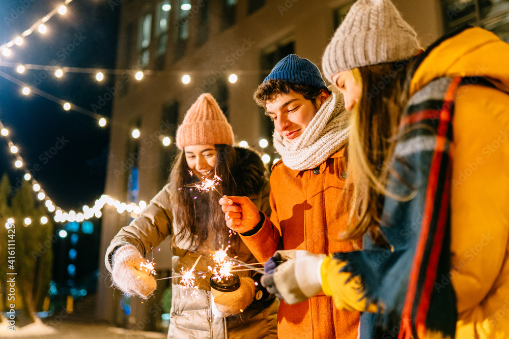 Happy girls and boy set fire to sparklers at night and laugh. Young people with beautiful lights. Girlfriends and boyfriend are travel. Rest during the holidays. Celebrating your life with fun.