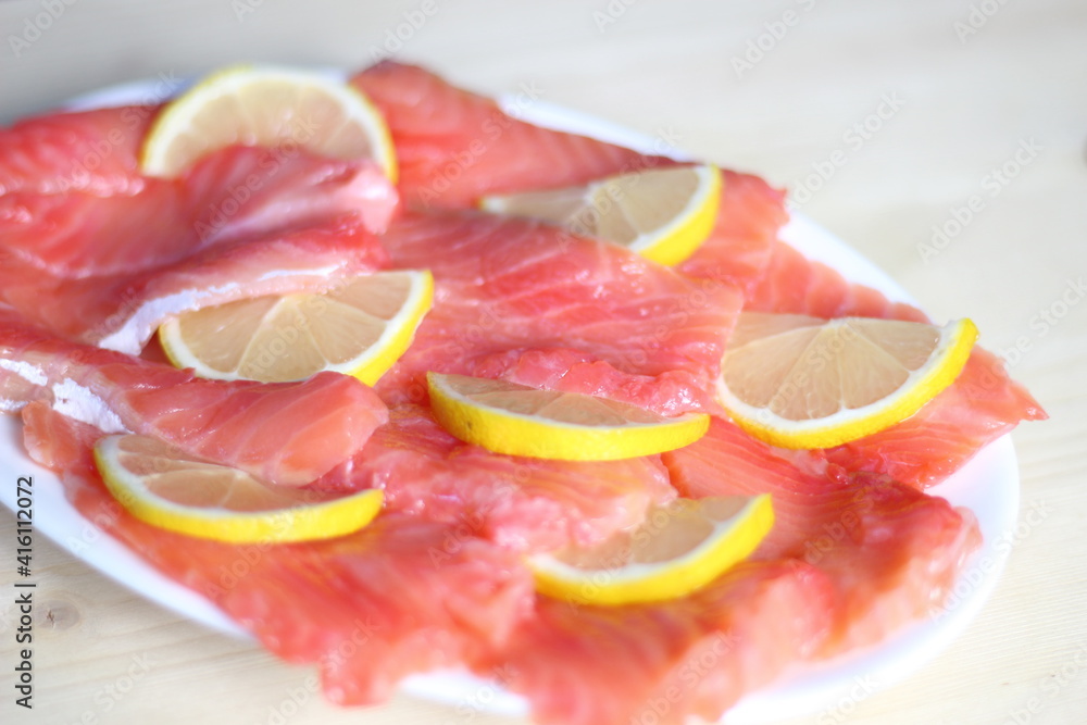 slices of salty red fish salmon with lemon on white plate on wooden background