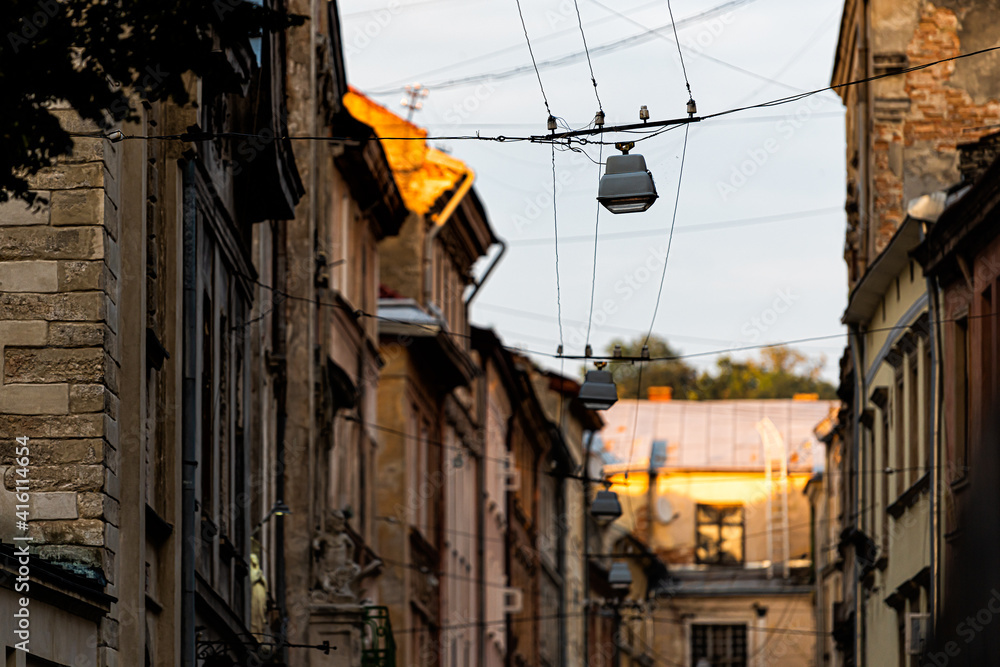Dark street narrow alley in Lviv, Ukraine, historic Ukrainian Lvov city during sunset with old vintage buildings in old town and hanging cables wires