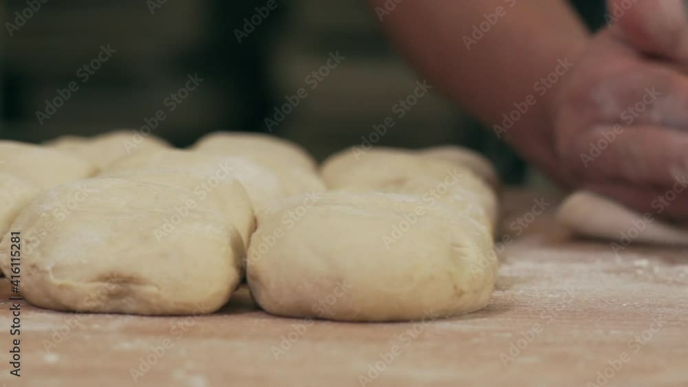 Skilled baker shaping dough to buns with his hands in slow motion. Traditional Austrian kaiser rolls being made in small bakery. Skilled baker shaping dough to buns with his hands in slow motion. Traditional Austrian kaiser rolls being made in small bakery.
