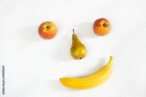 Funny face of fruit on a white background. Fresh fruit - apples, pears, bananas. The concept of proper nutrition, vegetarianism, fructarians, natural vitamins. Dishes, food for children. Top view. 