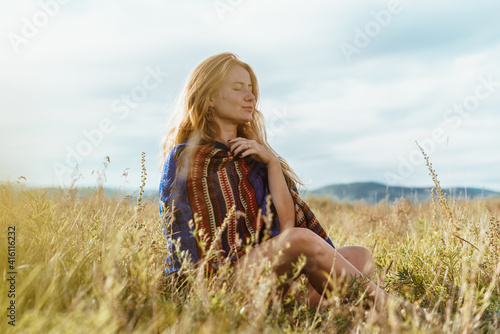 in the field sits and meditates a girl in loose hair in an ethno cape. High quality photo
