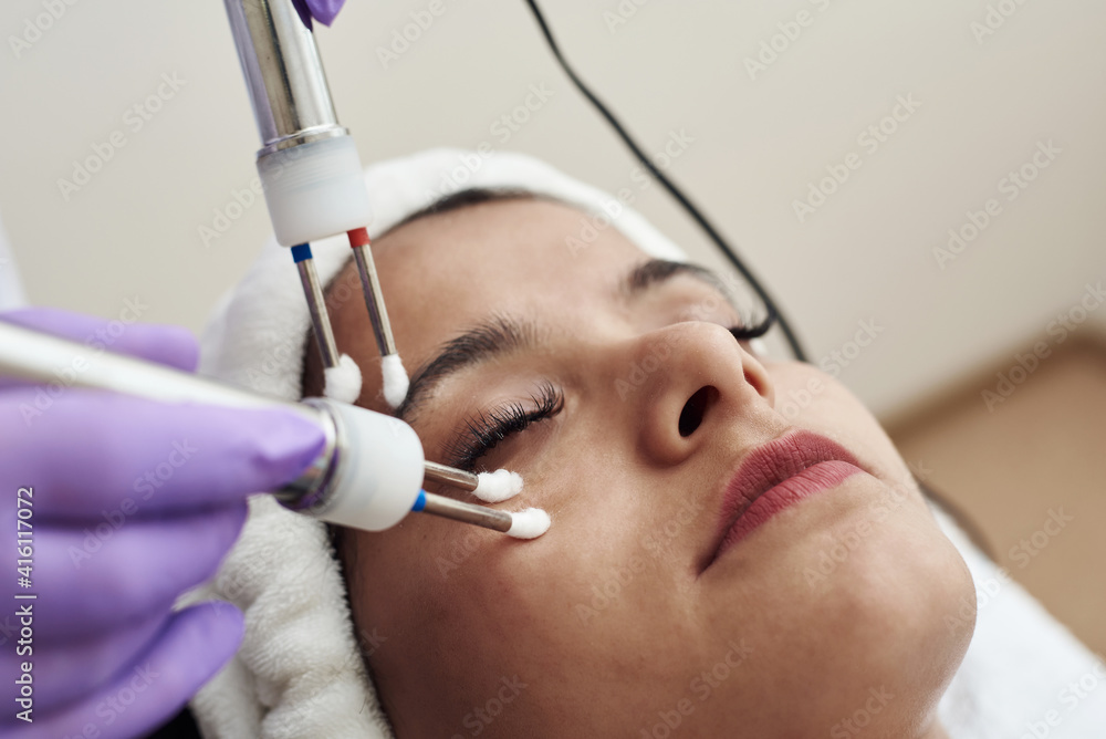 Naklejka premium Beautician using electrical impulses for healthy, firm, toned skin. Microcurrent medicine treatment. Beauty young woman