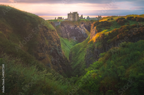 Golden sunrise or sunset light on the coastal landscape ruins of Donnottar Castle on the Aberdeenshire coast of Scotland. photo