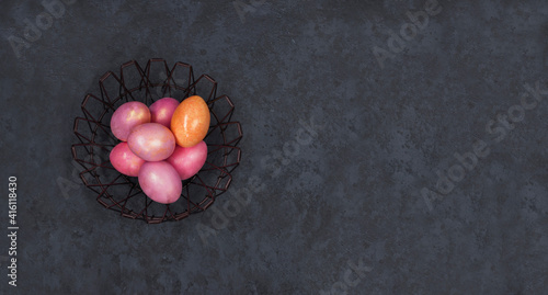 Concept of Easter holiday and spring. Banner. Easter multicolored pastel pink eggs in a metal basket on a dark background. Flat lay. Minimal style. Copy space