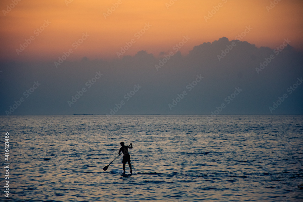 surfer rowing his board against cloudy sunset in background