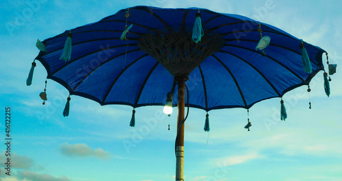 Asian traditional beach sun umbrella in the island of Bali in Indonesia before a vivid blue sunset sky in Summer holidays and exotic travel destination concept