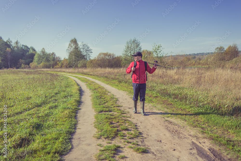 Fisherman walking along a rural road. Man travels on the road in nature