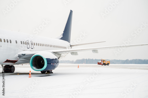 Side view of a passenger plane. A snowplow clearing snow from the runway is visible in the back.