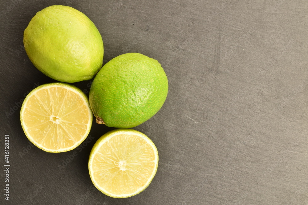 Two whole and two halves of natural lime, macro, on a serving plate of slate. Two whole and two halves of natural lime, macro, on a serving plate of slate.