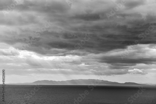 Black and white seascape with a dramatic sky and hills in the horizon