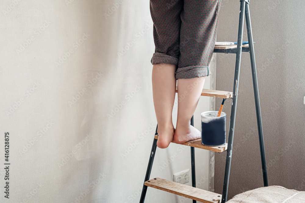 Woman with bare feet stained with white paint stands on stepladder. Home renovation concept Woman with bare feet stained with white paint stands on stepladder. Home renovation concept