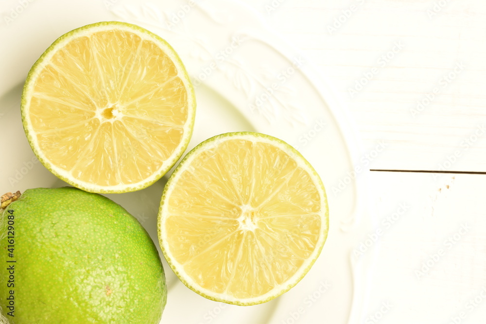 One whole and two halves of juicy lime on a white plate, close-up, on a painted wooden table. One whole and two halves of juicy lime on a white plate, close-up, on a painted wooden table.