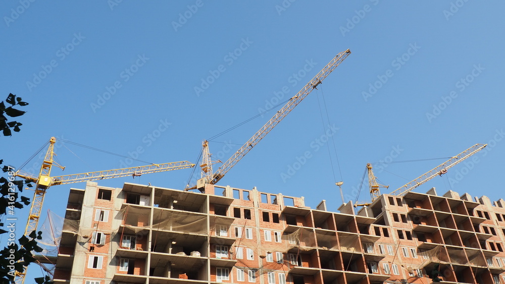 Working on place with many tall buildings under construction and cranes under a blue sky
