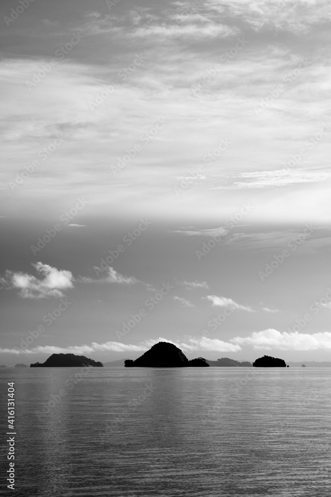 Black and white seascape with feathery clouds and a group of small islands in the horizon