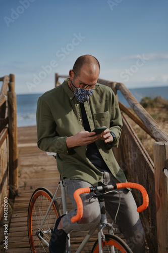 Adult man wearing face mask sitting in orange bike and using his phone.