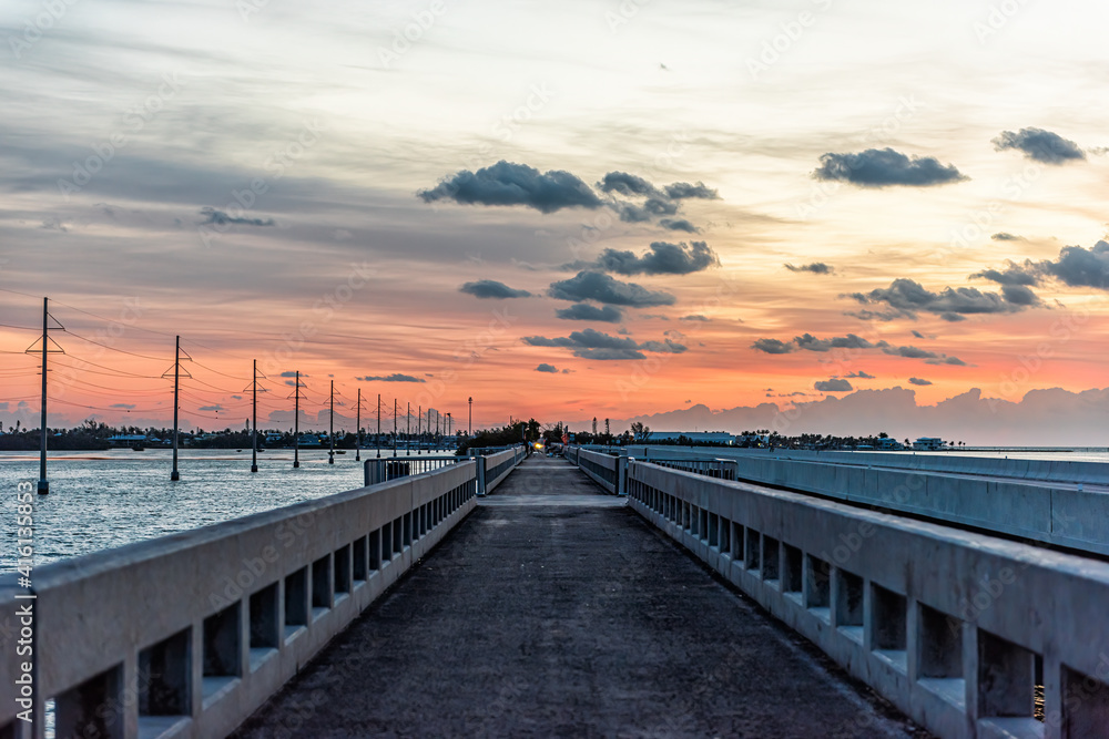 Cloudy sky at sunrise in Islamorada, Florida keys with colorful sky by overseas highway road of Gulf of Mexico with power lines and pedestrian bridge, people fishing