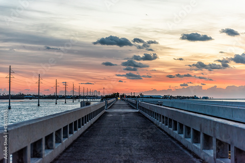 Cloudy sky at sunrise in Islamorada  Florida keys with colorful sky by overseas highway road of Gulf of Mexico with power lines and pedestrian bridge  people fishing