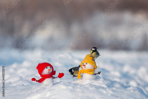 holiday greeting card with birds titmice sitting on cute snowmen in a winter park