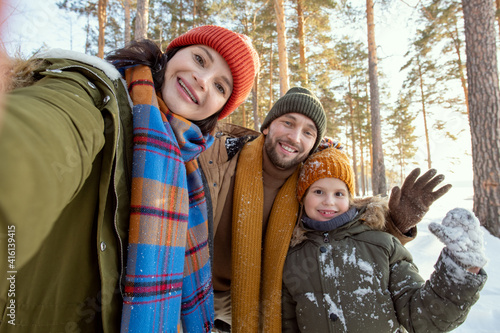 Happy young parents and their cute little daughter in winterwear making selfie