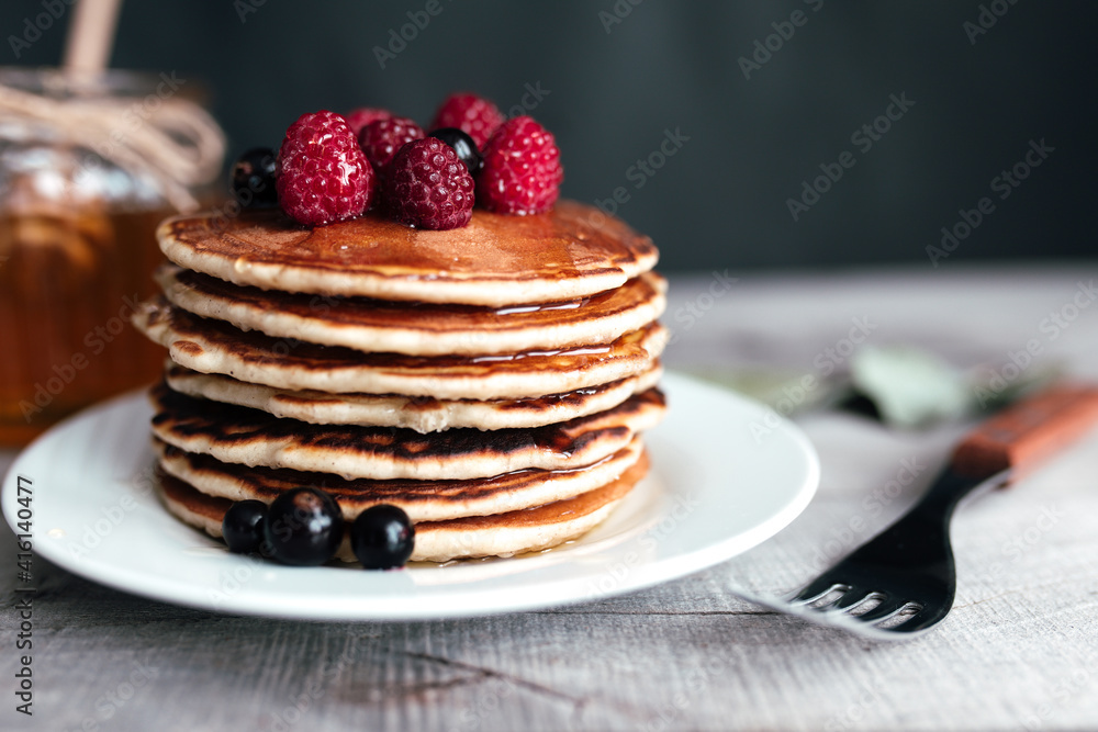 Juicy pancakes with berries and honey on a white plate, spoon, jar, wooden table Juicy pancakes with berries and honey on a white plate, spoon, jar, wooden table