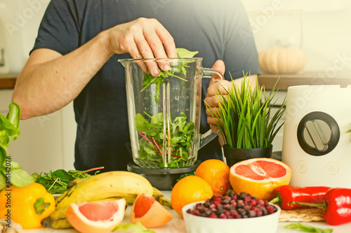 A man prepares a wellness food smoothie with fresh herbs, bananas and fresh berries in a blender 