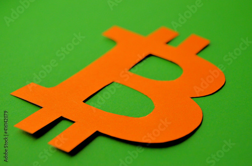 The bitcoin sign carved from orange paper lies on a green background close-up. High quality photo