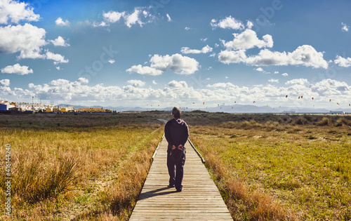 Man walking along a wooden boardwalk through grassland