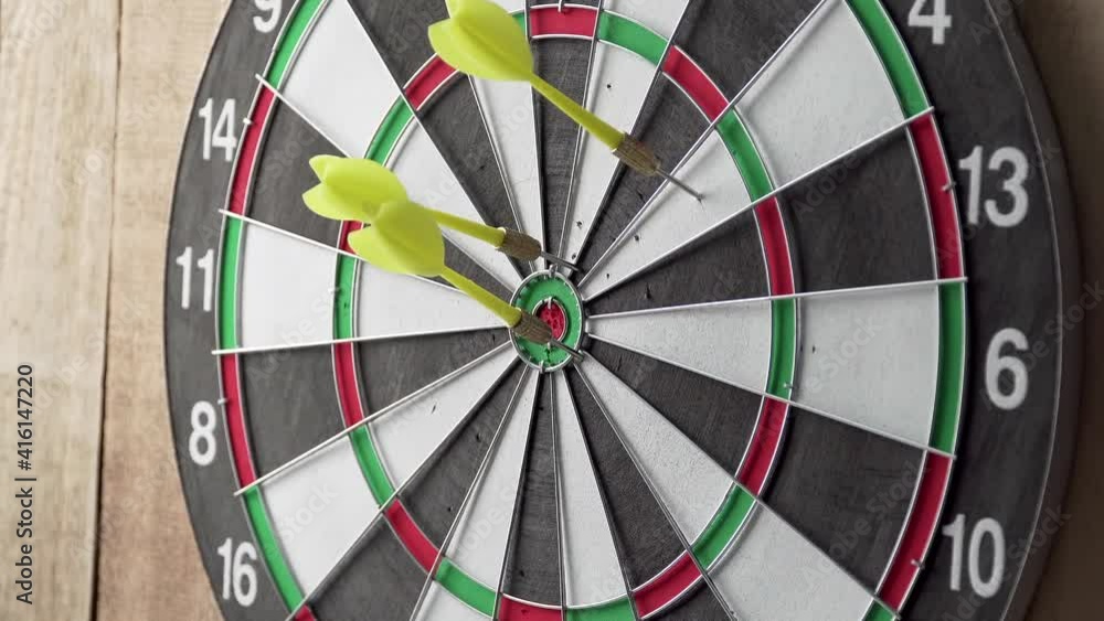 Darts game. Throwing darts at the target. A somebody throw the darts on the dart board. Three yellow darts hit the target. Dart board hanging on a wooden wall Darts game. Throwing darts at the target. A somebody throw the darts on the dart board. Three yellow darts hit the target. Dart board hanging on a wooden wall