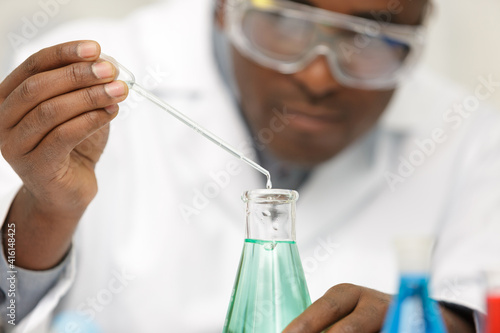 young smiling chemist in googles holding purple liqiud
