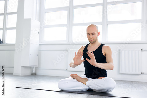 yoga man sits on mat on floor training correct yoga breathing, handsome calm bald male engaged in yoga