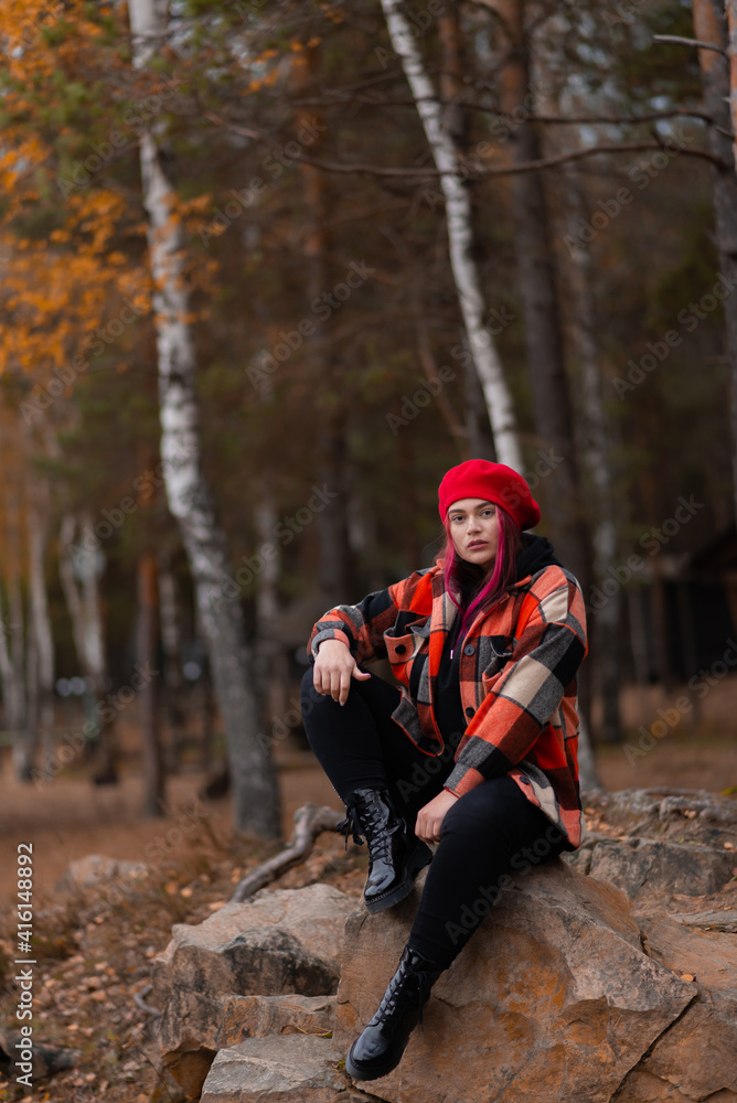 Confidently looking girl is sitting on a rock in an autumn forest. Confidently looking girl is sitting on a rock in an autumn forest.