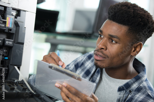man technician writing down on clipboard while repairing printer