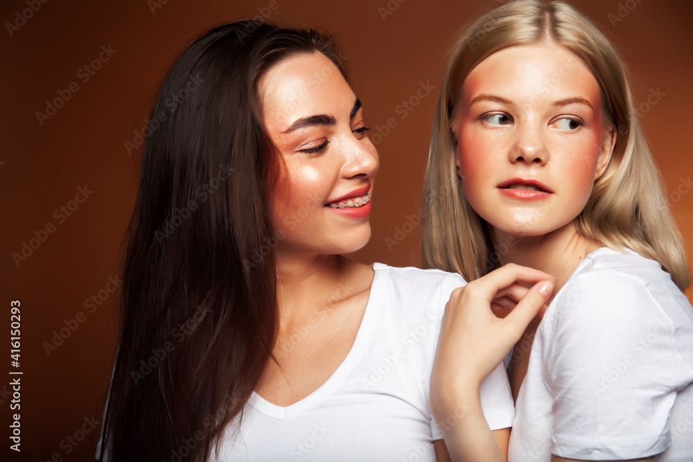 two pretty diverse girls happy posing together: blond and brunette, caucasian and asian on brown background, lifestyle people concept two pretty diverse girls happy posing together: blond and brunette, caucasian and asian on brown background, lifestyle people concept